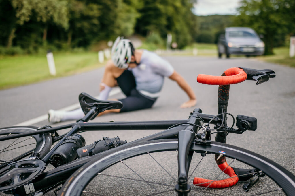 Injured cyclist sitting in pain next to the racing bicycle