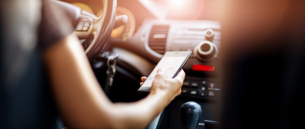 distracted driver at steering wheel with smartphone in her hand.