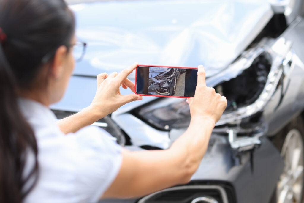 Woman takes pictures of damage to car after accident by smartphone. 