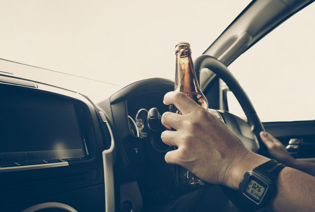 A driver holding alcoholic bottle while driving / Drunk driving concept