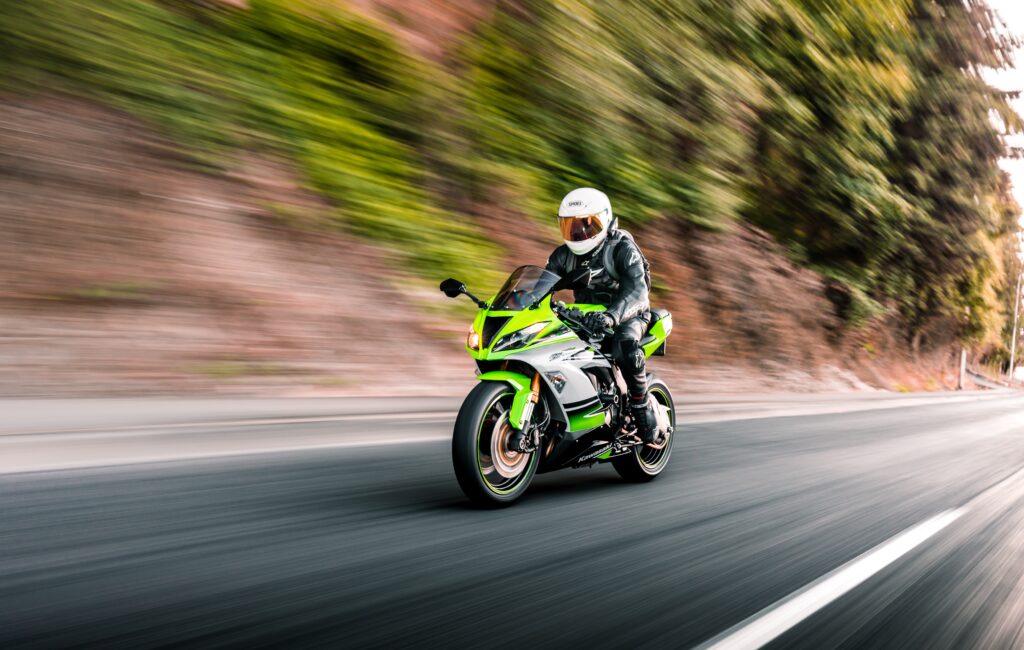Green Kawasaki motorcycle being driven on the streets with trees in the background