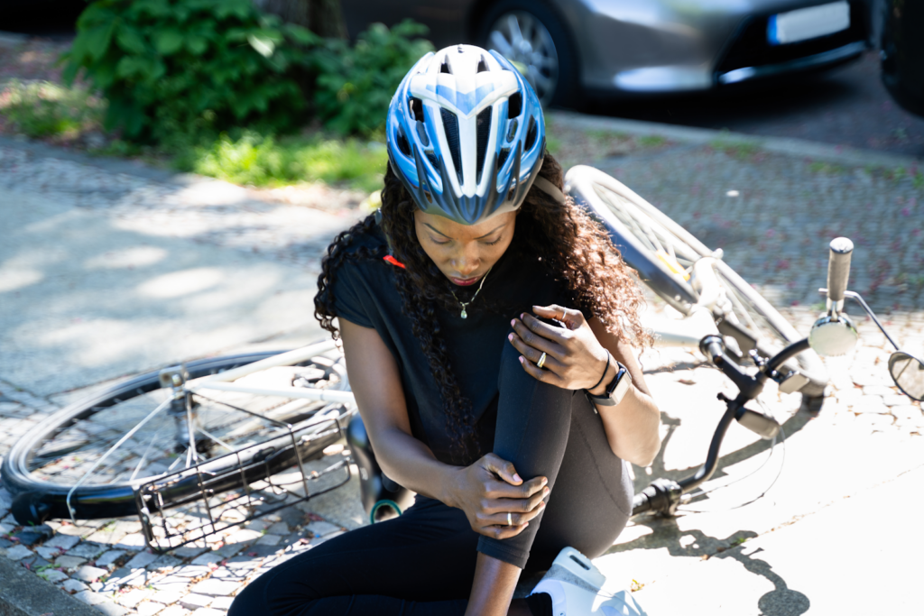 woman holding her knee with her bike laying beside her after a bicycle accident