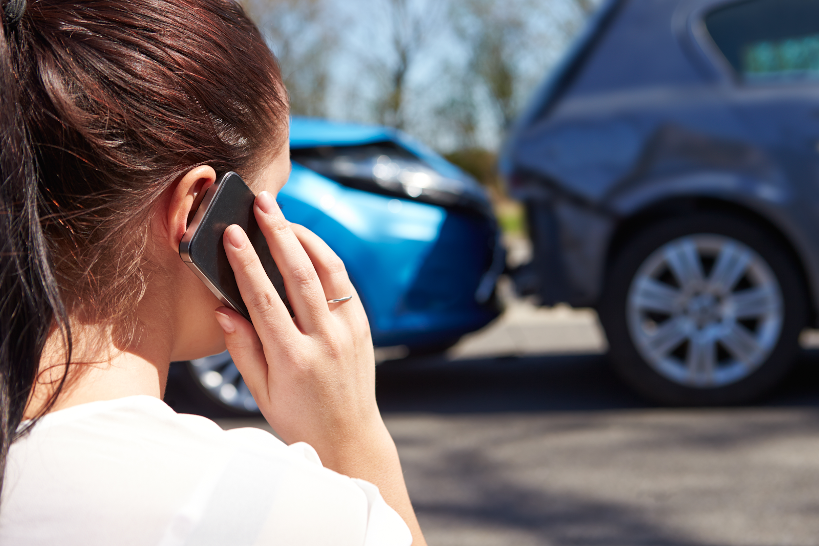 woman calling her insurance company to file a claim after an uninsured motorist accident, she is looking at the car rear ending the other