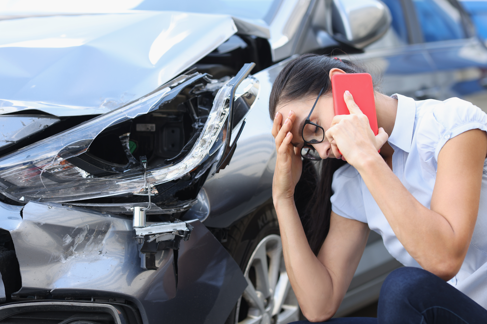woman on the phone looking at the damage of her car, in need of compensation