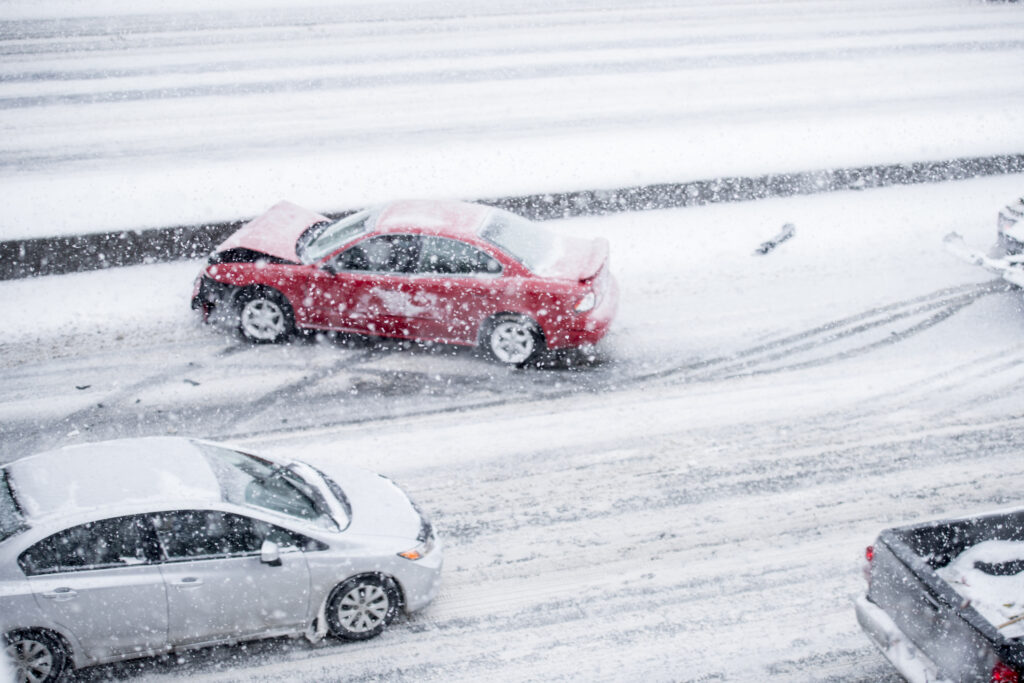 A red car with front-end damage on the side of the freeway during a snowstorm. 