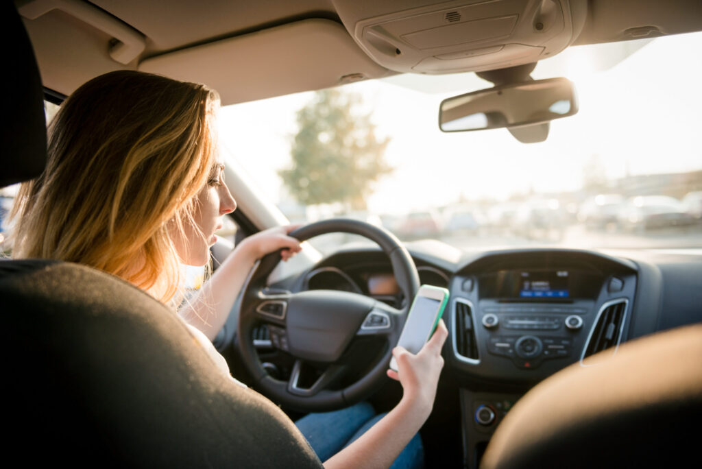 A woman checks her phone for messages while driving her car and not paying attention to the road. 