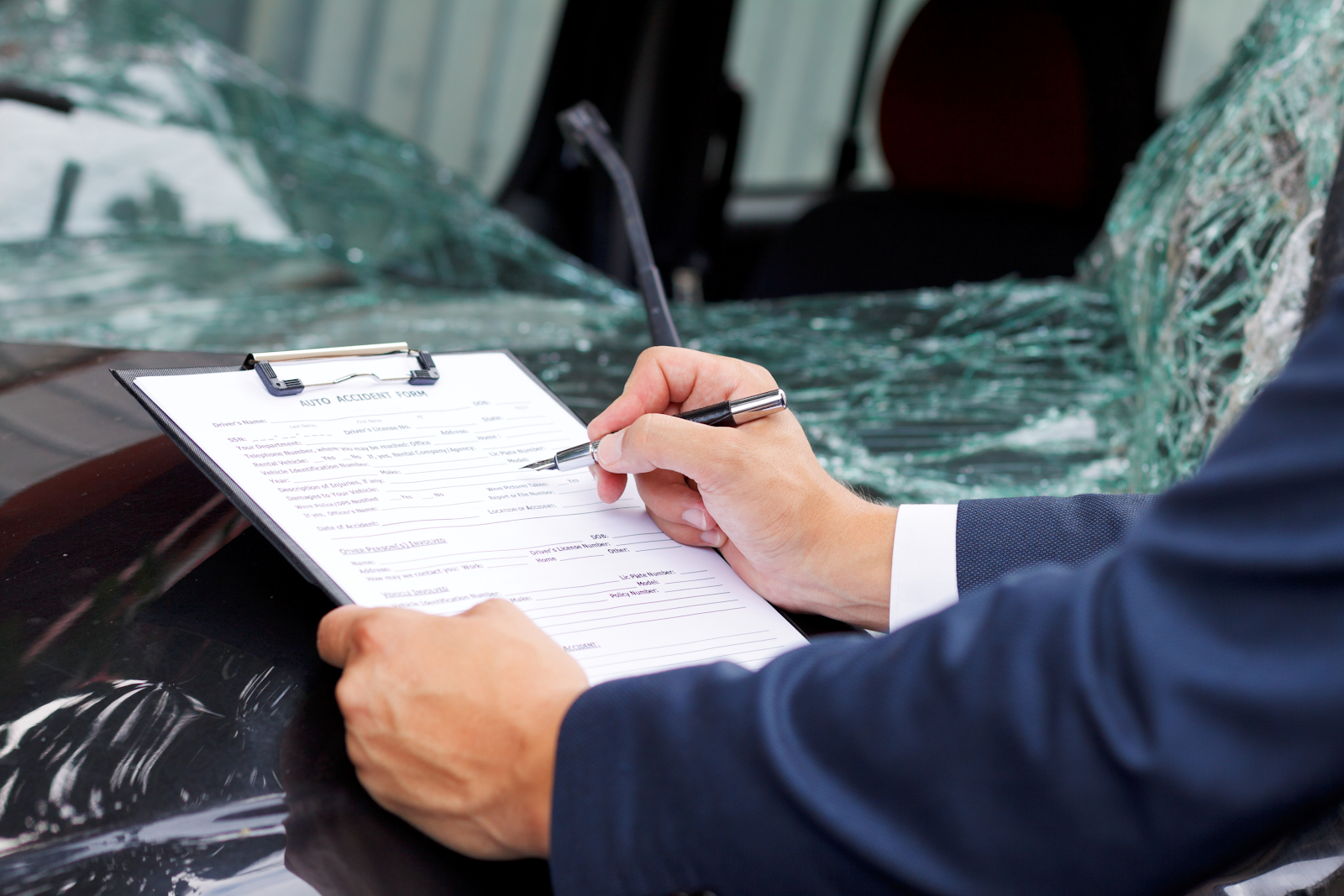 car accident lawyer writing on a clipboard on top of a damaged car after an accident