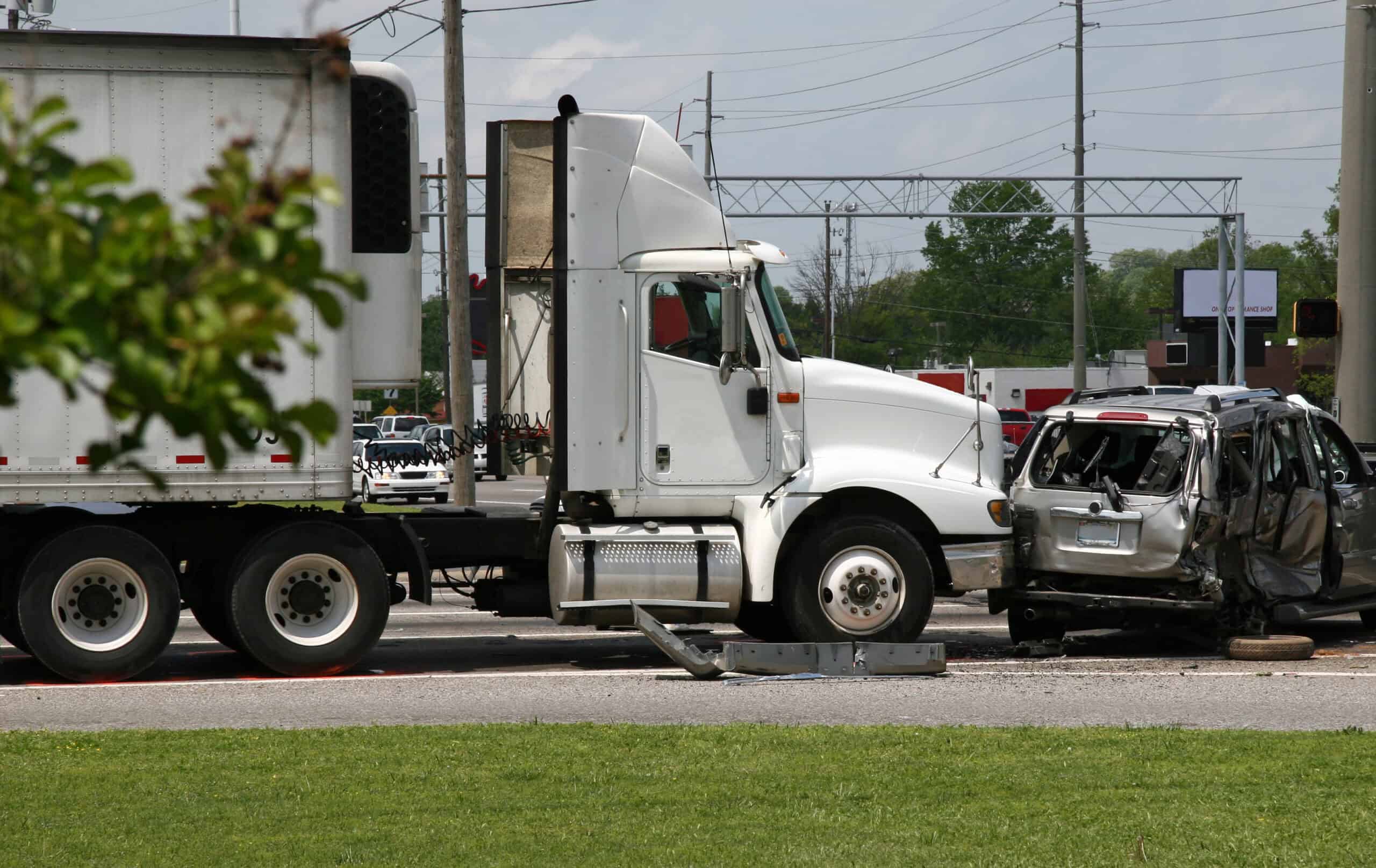 A gray minivan with heavy damage after it is involved in a crash with a large, white 18-wheeler.