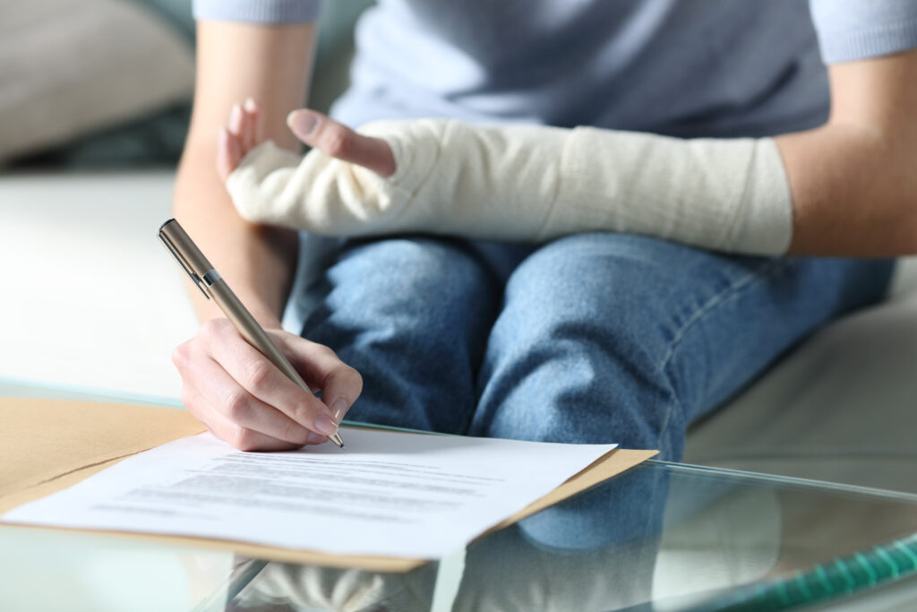 A person with a bandaged arm reviews and signs documents related to her personal injury claim.
