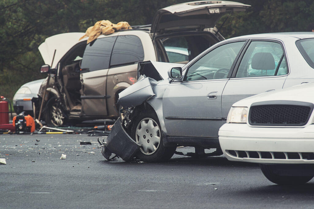 A multi-car accident with damages to vehicles and a police officer arriving on the scene.